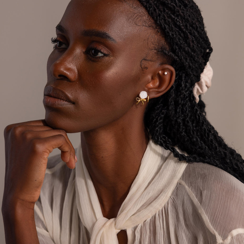 Profile view of a woman with white rose and gold bow earrings with a pearl stud and huggie hoop to complete the look.