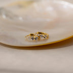 Lace Diamond Huggies—gold hoop earrings adorned with small clear gemstones—are elegantly displayed on a glossy, light-colored dish.