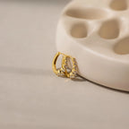 The Lace Diamond Huggies, elegant earrings with embedded crystals, rest against a beige curved ceramic dish, echoing the timeless style of classic diamond hoops.