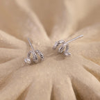 Pair of silver Twisted Snake Earrings displayed on a sandy-textured surface