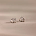 A pair of Twisted Snake Studs, silver and spiral-shaped, displayed on a soft beige surface with a blurred background—ideal for those who love elegant serpentine-inspired jewelry.