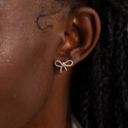 Close-up of model wearing a gold pavé bow stud earring, sparkling with tiny diamond stones and styled in a dainty ribbon shape.