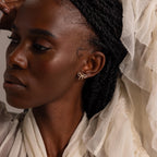 Model wearing gold pavé bow stud earrings, styled with a textured ivory blouse and soft natural lighting for an elegant, feminine look.