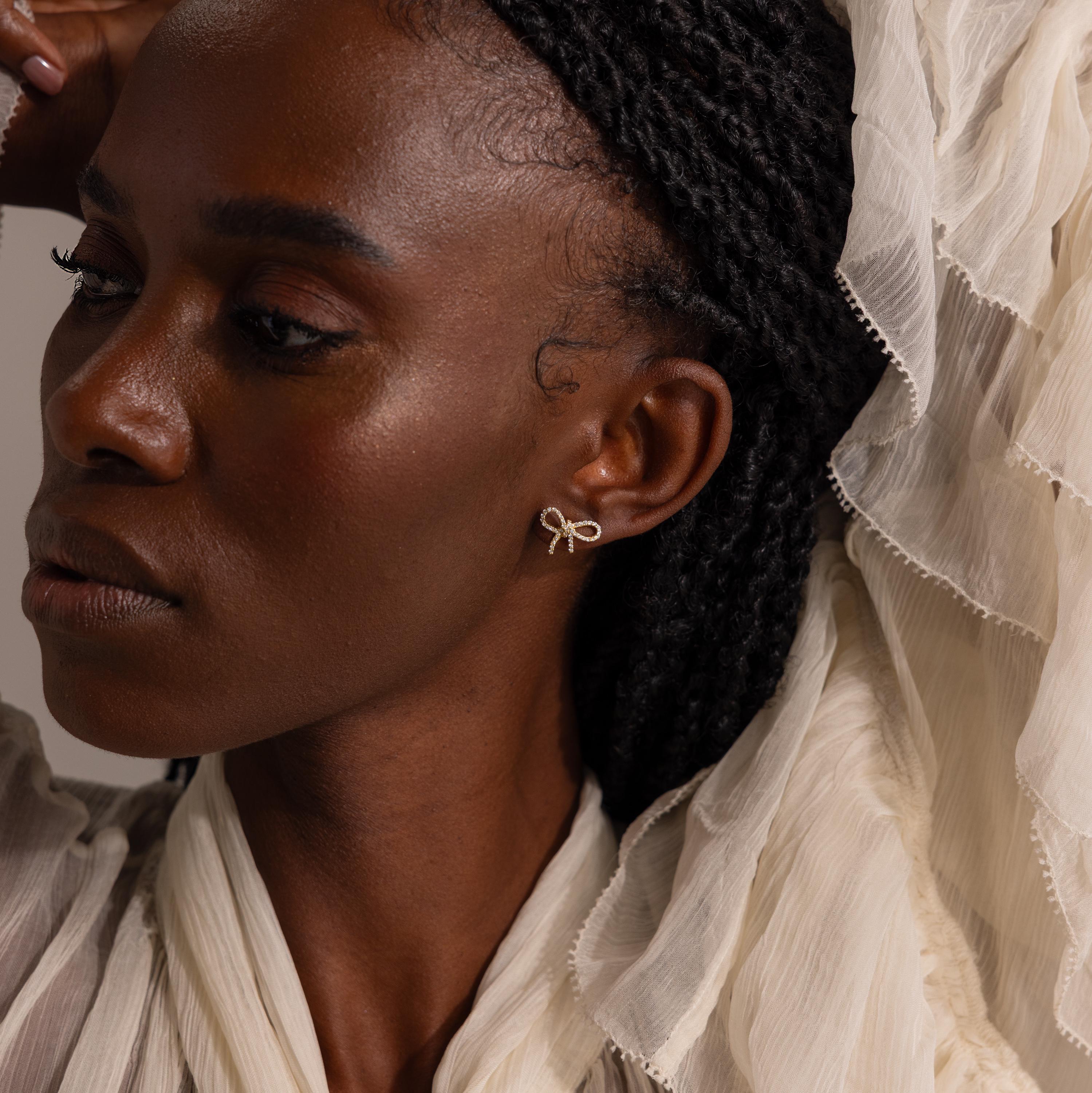 Model wearing gold pavé bow stud earrings, styled with a textured ivory blouse and soft natural lighting for an elegant, feminine look.