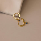 Ivy Birthstone Hoops—gold hoop earrings with small blue flower charms—add a delicate touch to any look, shown here on a light beige surface.