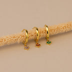 Three Ivy Birthstone Hoops, each featuring gold hoops with vibrant butterfly charms, are displayed on a beige textured rod against a neutral background—perfect as personalized jewelry.