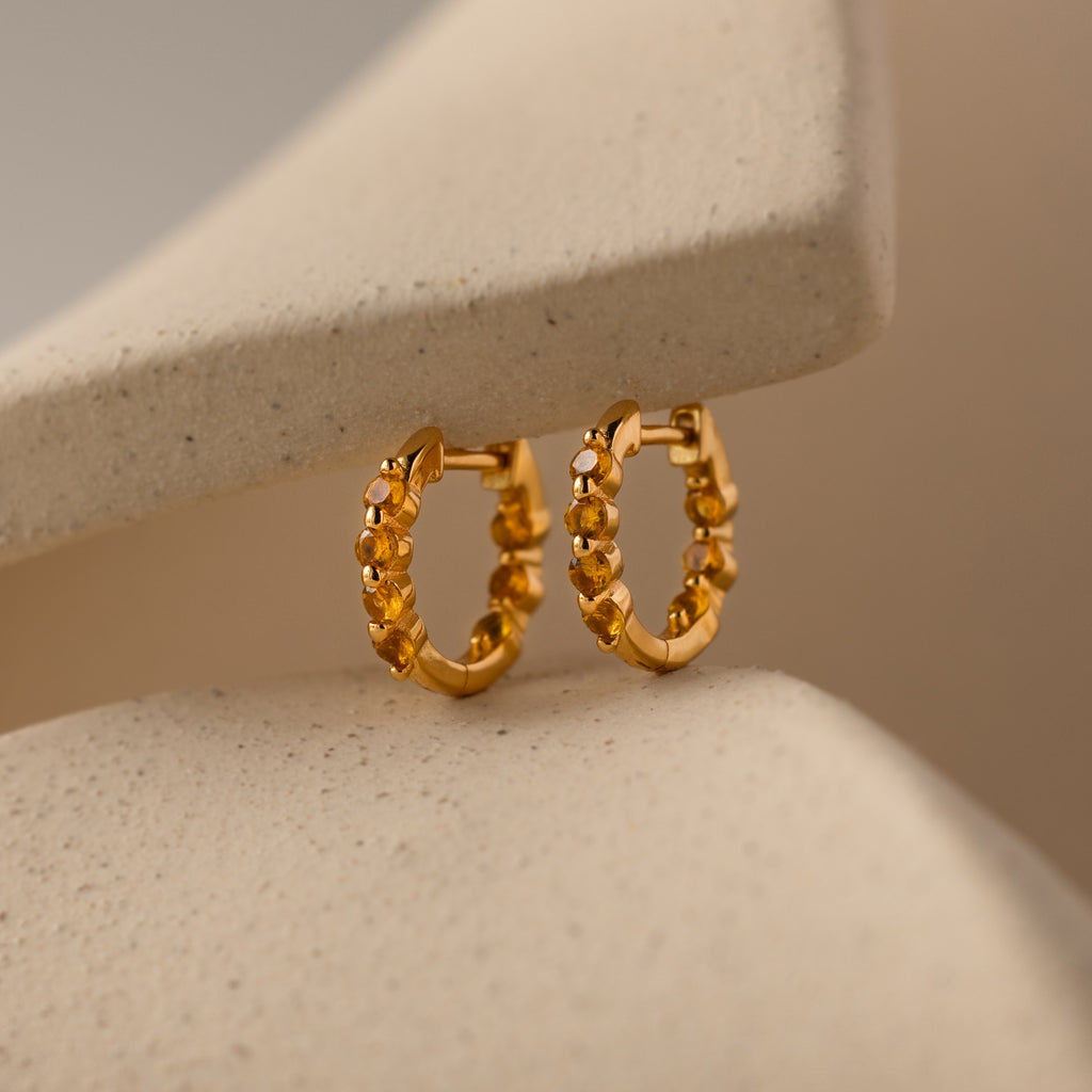 Mini Topaz Beaded Huggies shown on a soft beige curved background—ideal for those who appreciate modern huggie earrings with timeless elegance.