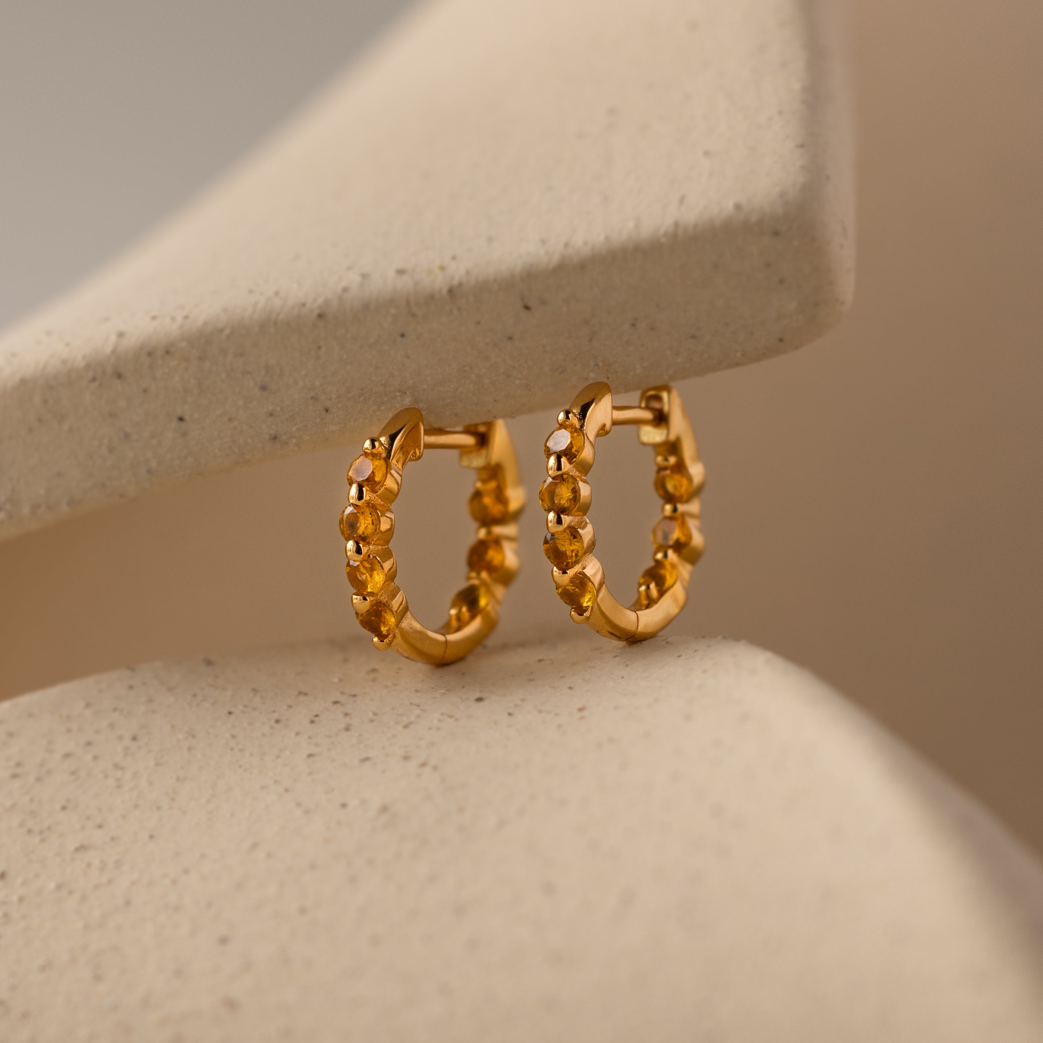 Mini Topaz Beaded Huggies shown on a soft beige curved background—ideal for those who appreciate modern huggie earrings with timeless elegance.