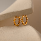 Mini Birthstone Beaded Huggies with a textured design shine against a soft beige background—add a unique touch of birthstone jewelry elegance to your look.