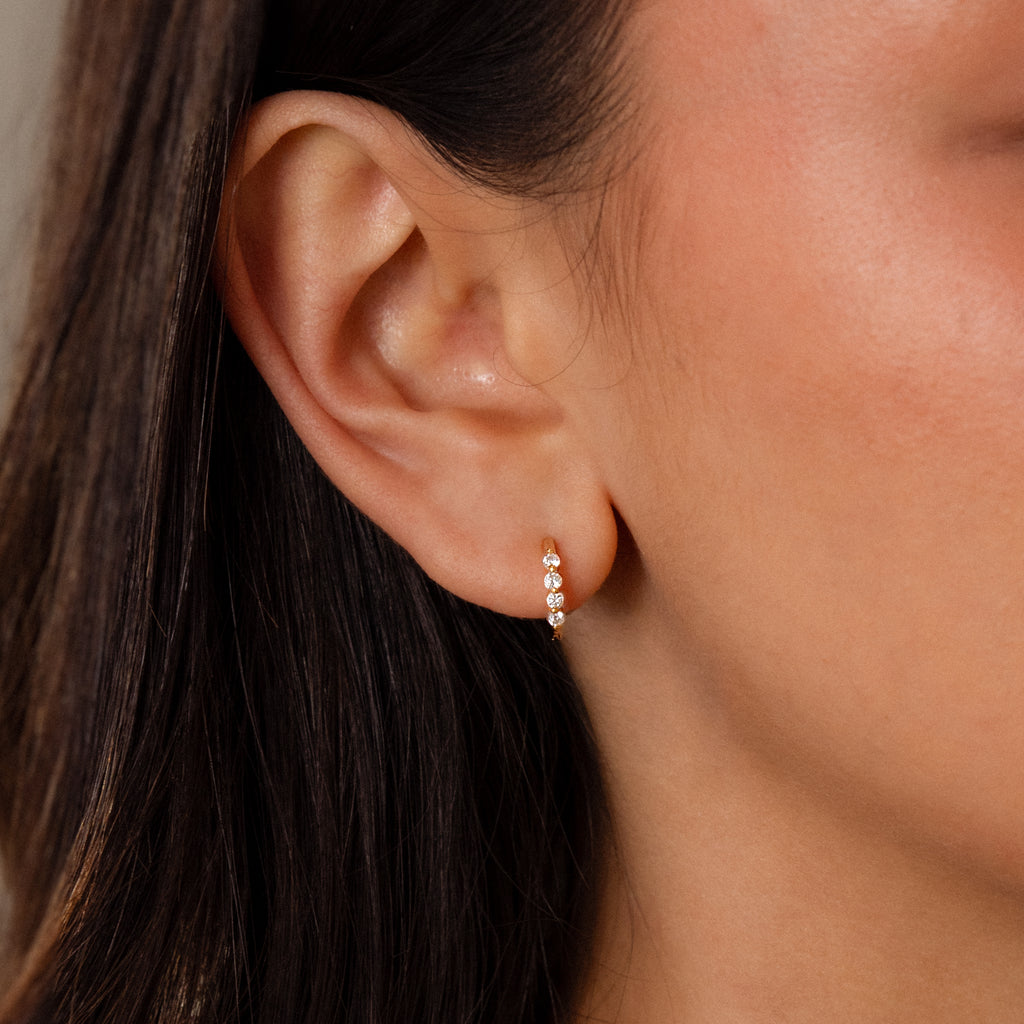 Close-up of a womans ear wearing Mini Diamond Beaded Huggies—stylish gold hoops adorned with three sparkling diamonds.