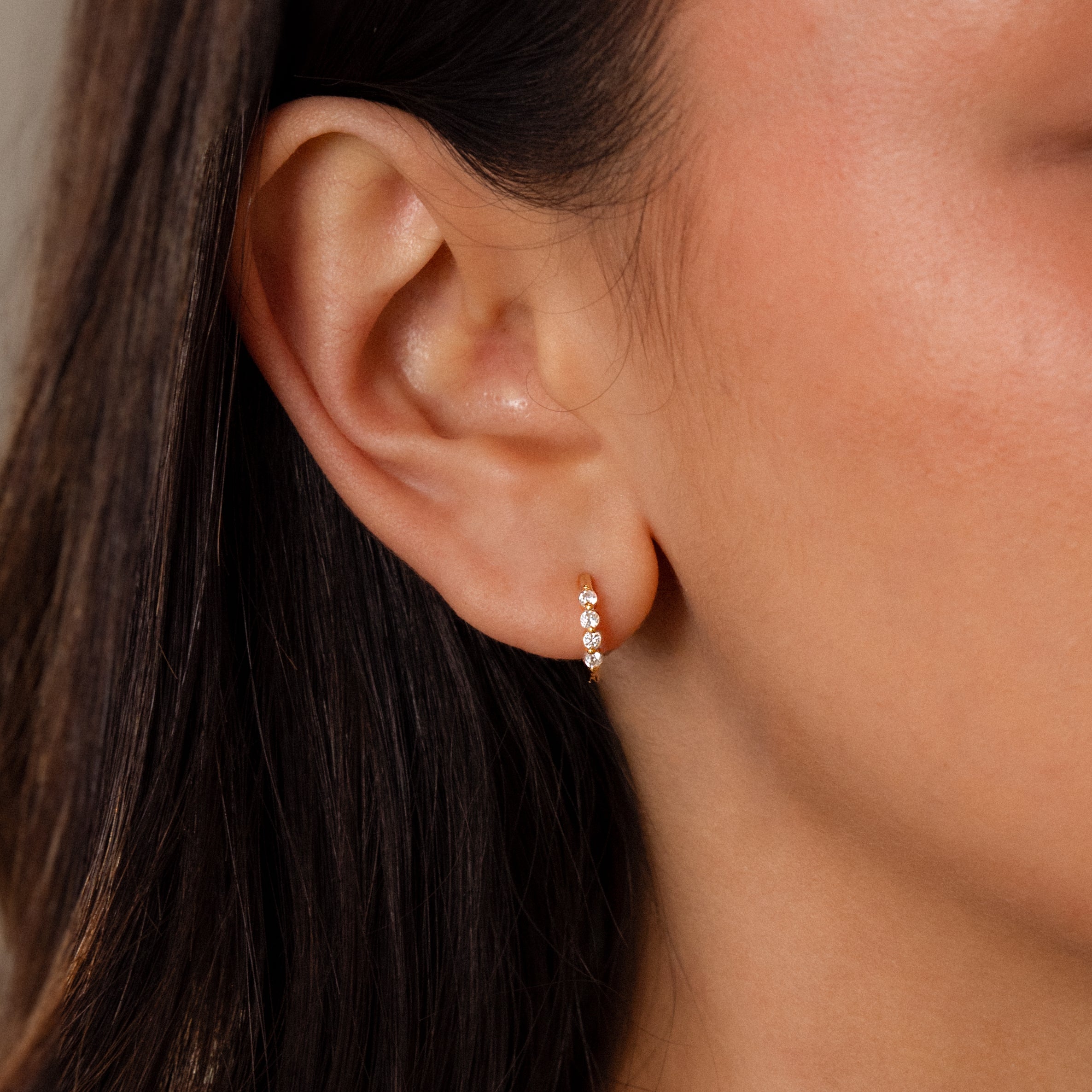 Close-up of a womans ear wearing Mini Diamond Beaded Huggies—stylish gold hoops adorned with three sparkling diamonds.