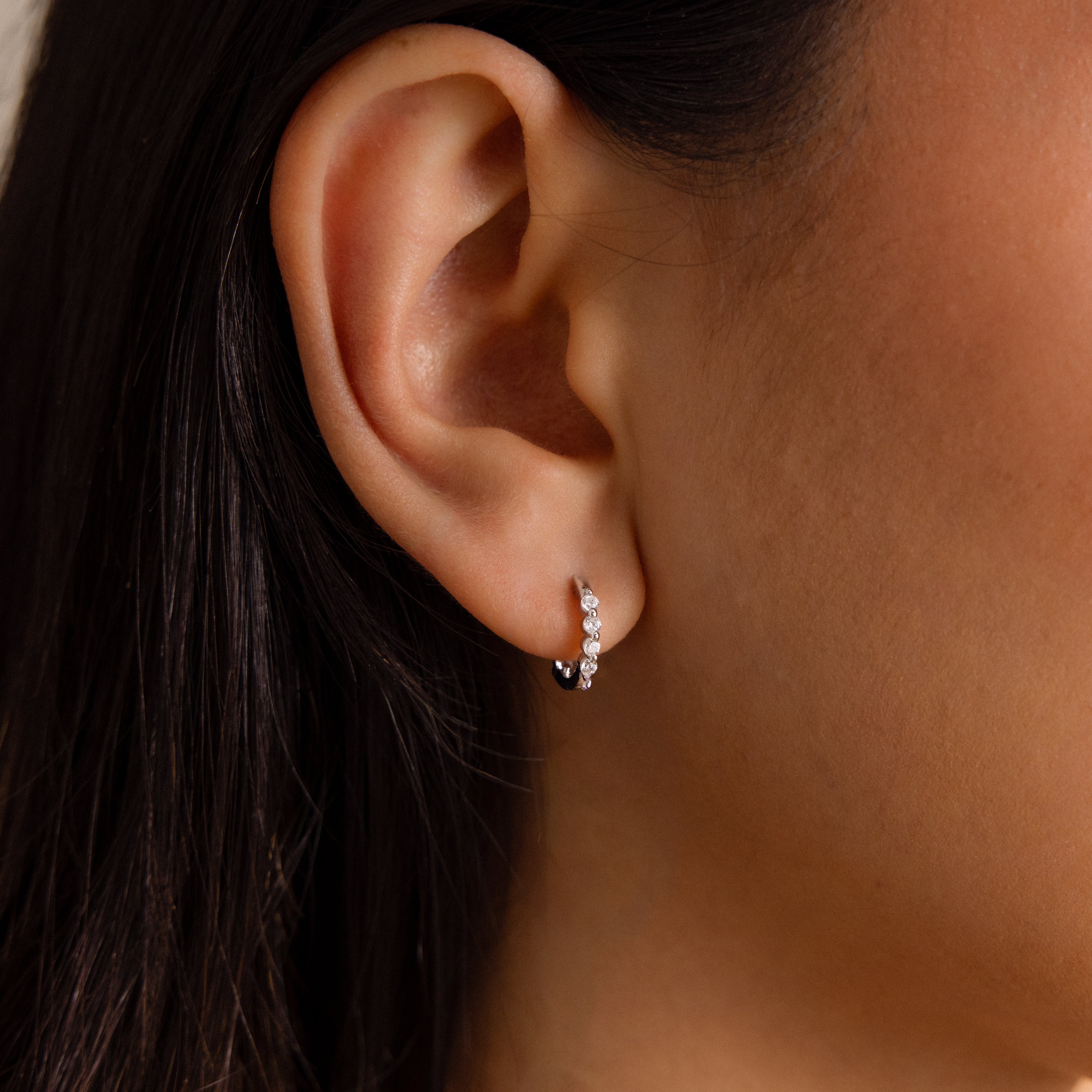 Close-up of a womans ear wearing Mini Birthstone Beaded Huggies—dainty silver hoops with three sparkling birthstones.