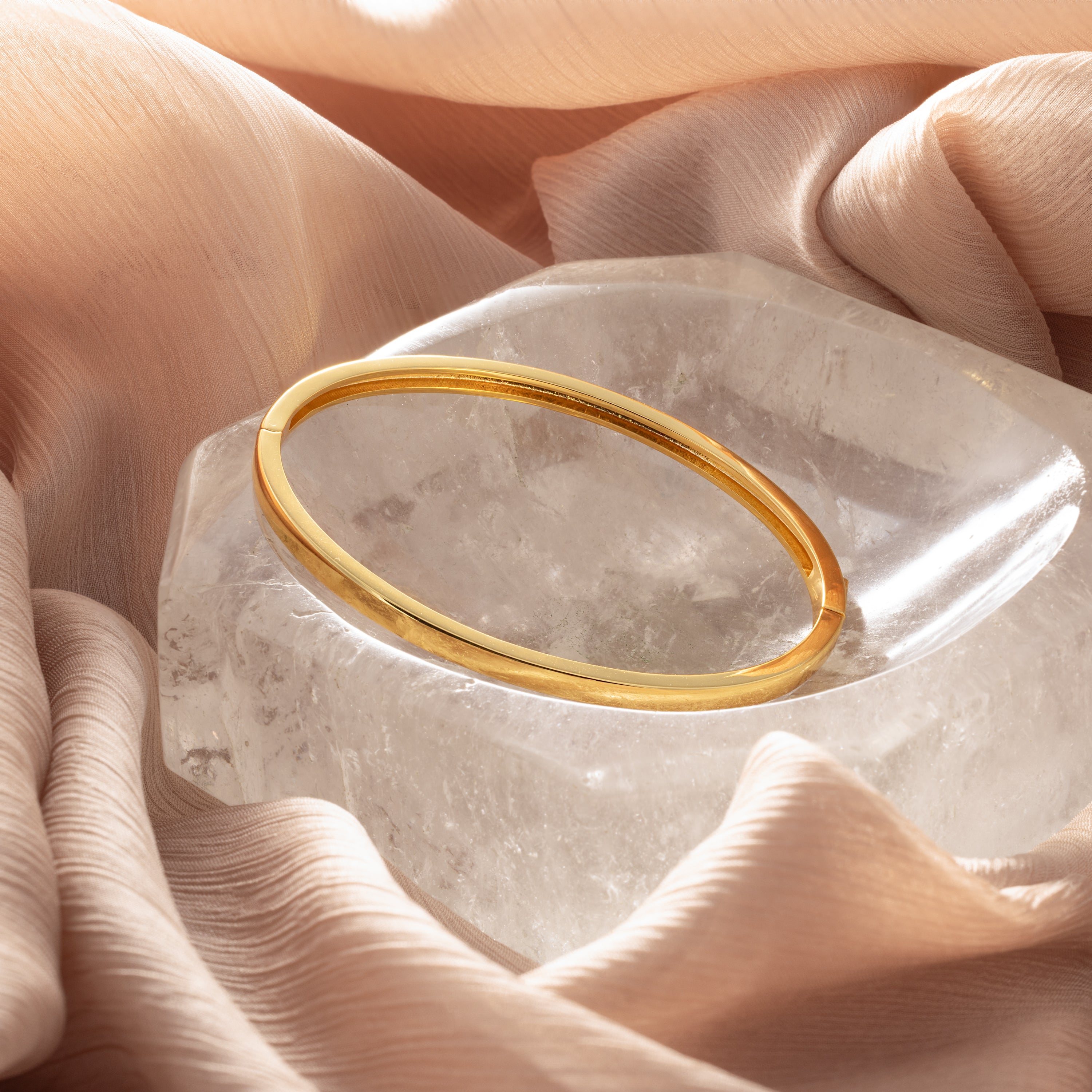 The Classic Bangle is showcased on a clear crystal and soft beige fabric, creating an elegant and chic jewelry display.