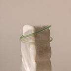Two thin jade bangles in soft translucent green tones placed on a stone display.
