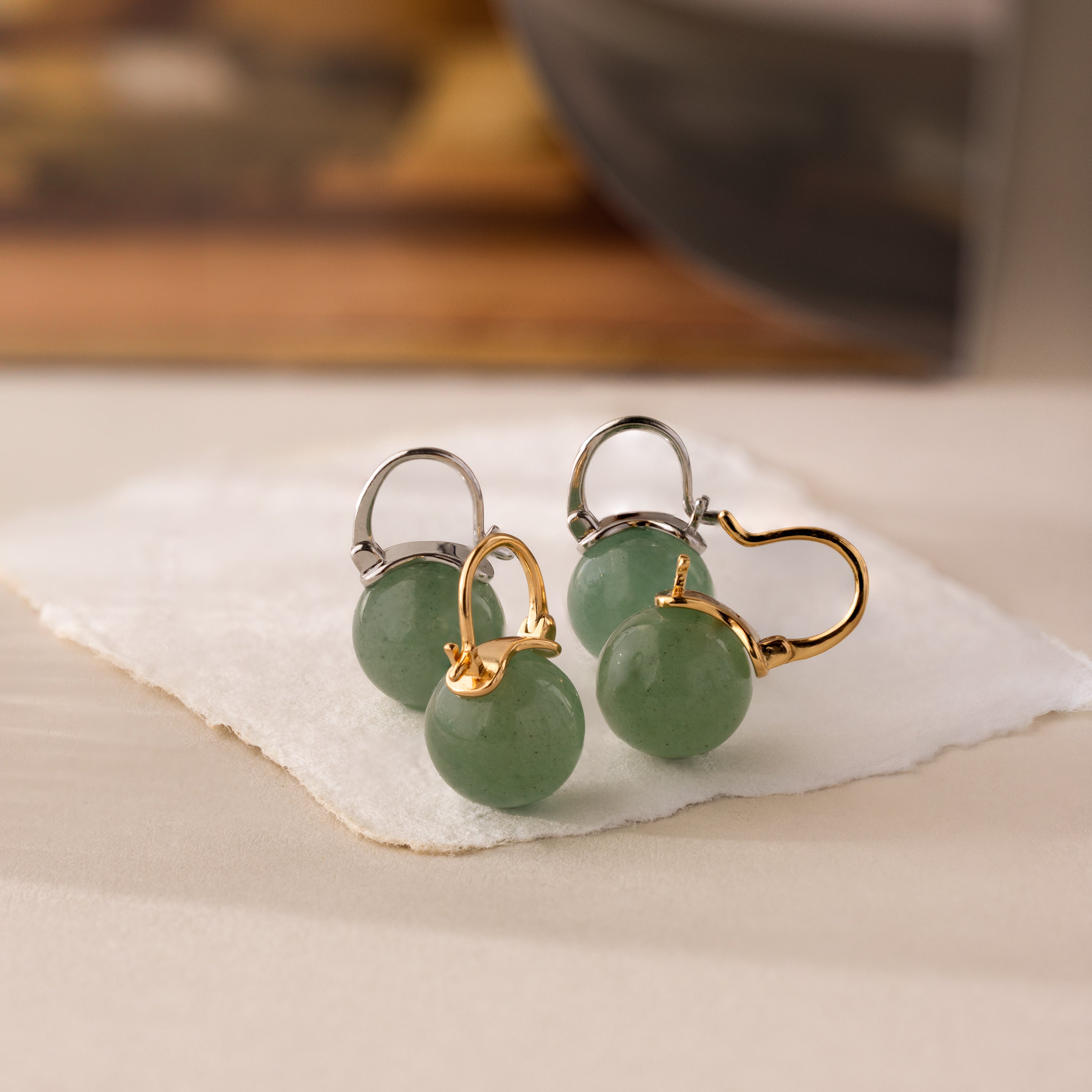 Close-up of two pairs of Jade Dome Drop Earrings in gold and silver, each featuring rounded green gemstones on dainty hoops, sitting up right.