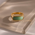 Close-up of a gold signet ring with a polished green jade gemstone inlay, displayed on a glass surface.