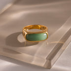 Close-up of a gold signet ring with a polished green jade gemstone inlay, displayed on a glass surface.