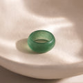 Close-up of a thick green jade gemstone statement ring with a smooth, glossy finish, displayed on a neutral surface.