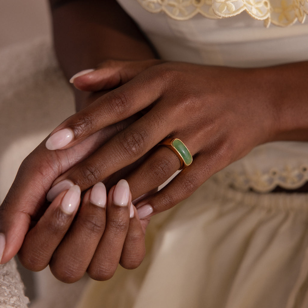 Model wearing a gold signet ring with a polished green jade gemstone inlay.