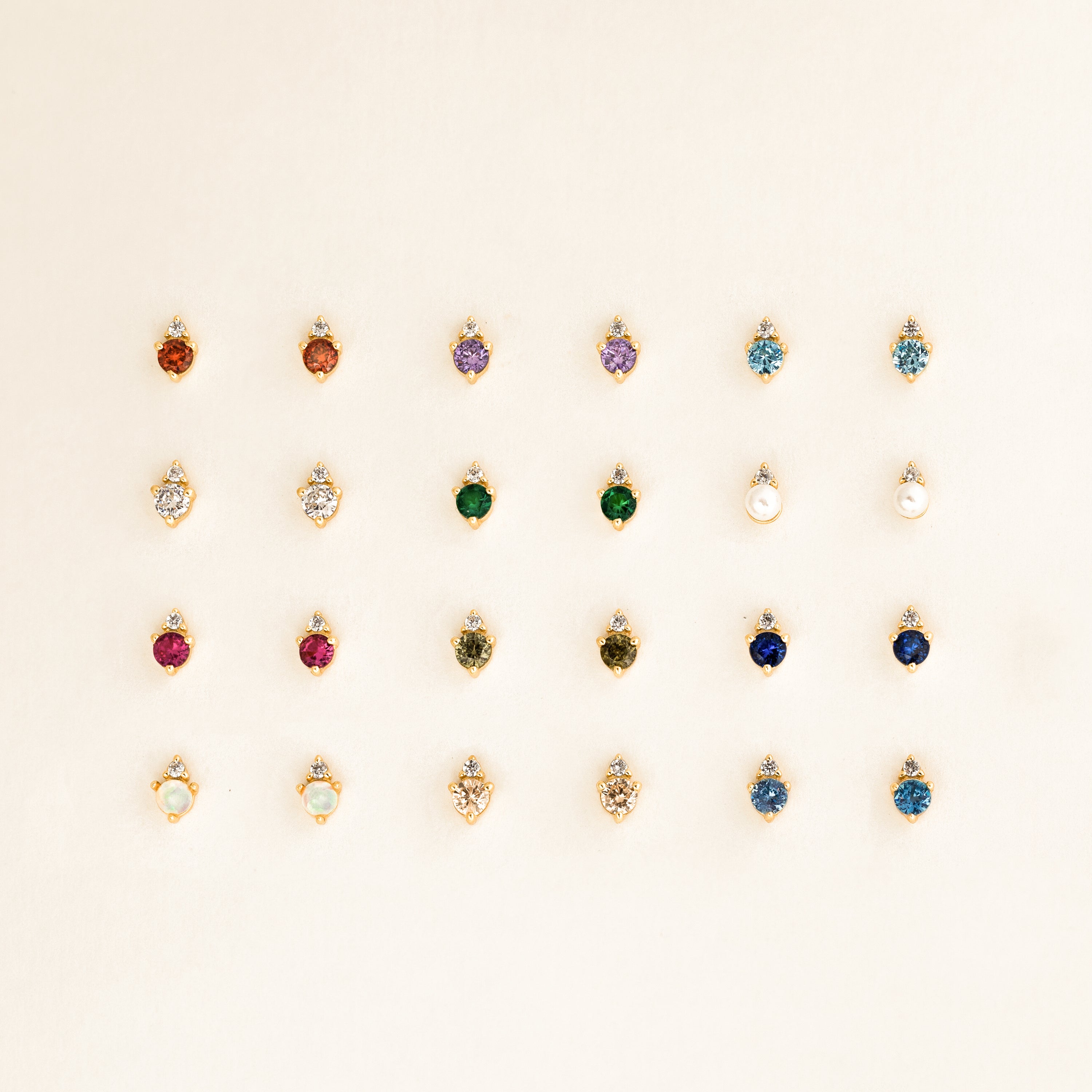 Twenty-four pairs of Raindrop Opal Studs are arranged in four rows on a light beige background.