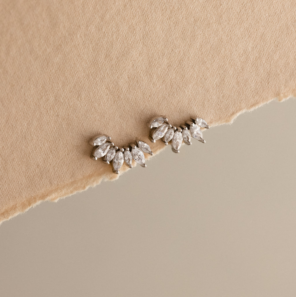 Marquise Diamond Arc Climbers in Silver, leaf-shaped ear climbers inspired by marquise diamonds, displayed on torn beige fabric with a neutral background.