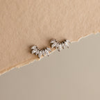 Marquise Diamond Arc Climbers in Silver, leaf-shaped ear climbers inspired by marquise diamonds, displayed on torn beige fabric with a neutral background.