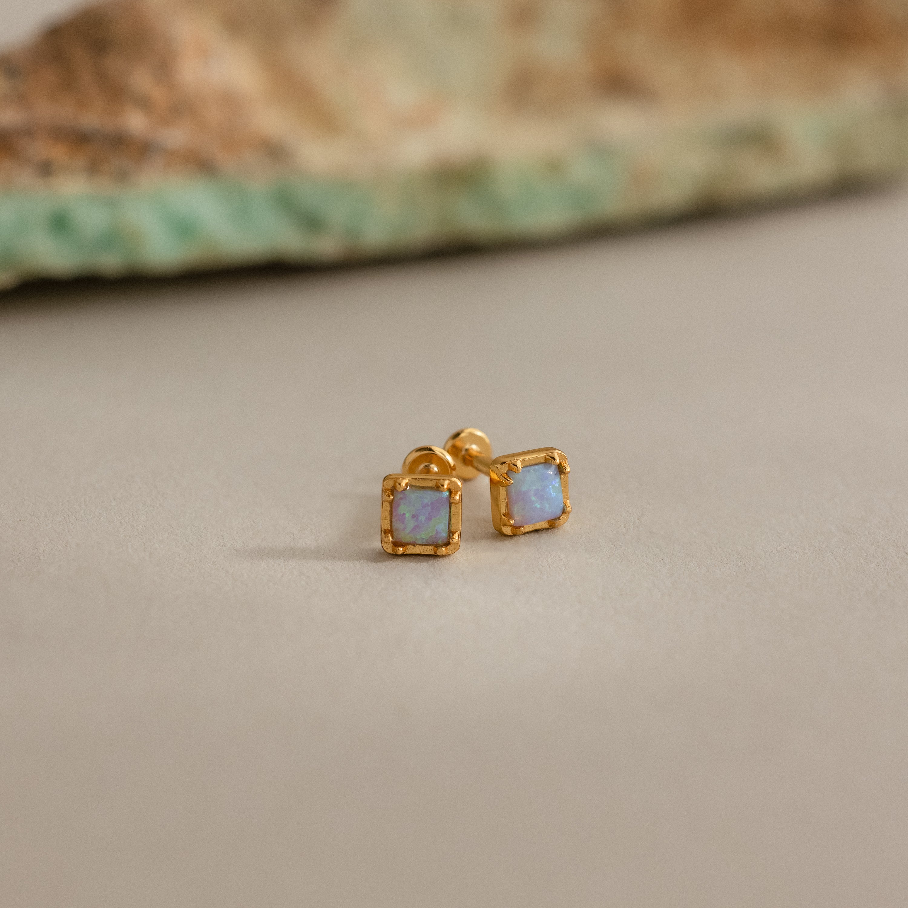 Blue Opal Prism Studs in 18K Gold feature iridescent blue opals set in gold, displayed on a neutral surface with a softly blurred background.