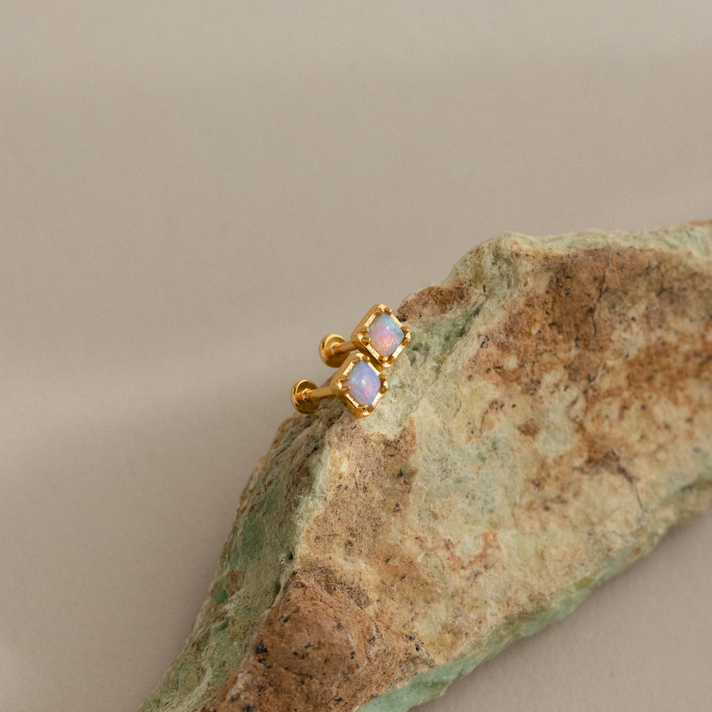 Blue Opal Prism Studs in 18K Gold, featuring two opal stones each, displayed on a textured rock with a neutral backdrop—ideal for fans of iridescent jewelry.