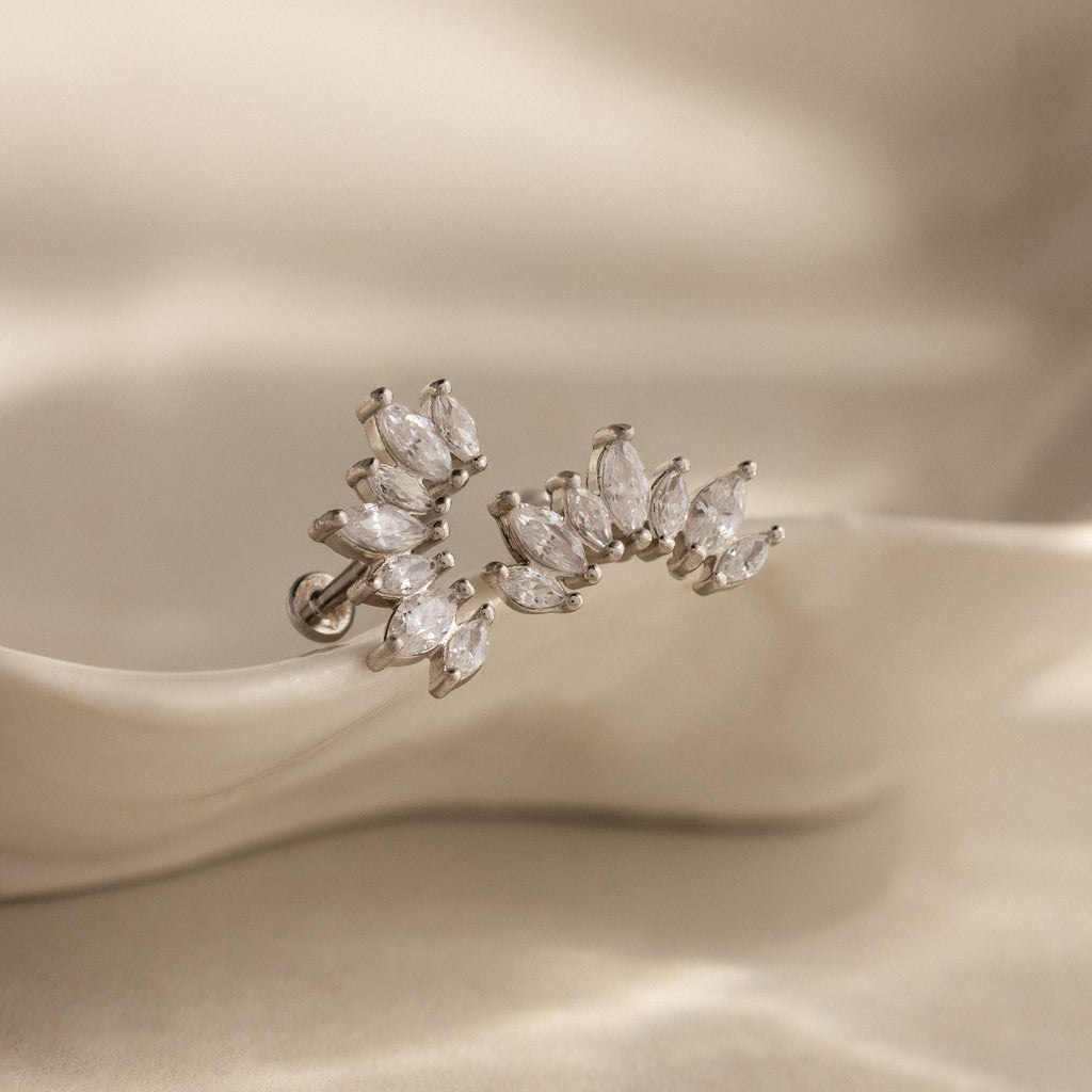 The Marquise Diamond Arc Climbers in Silver ear cuff, featuring marquise stones, rests on a smooth, cream-colored surface.