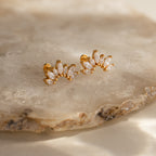 Marquise Diamond Arc Climbers in 18K Gold, featuring marquise-shaped clear stones in a leafy design, displayed on a light stone surface—a stunning update on classic marquise earrings.