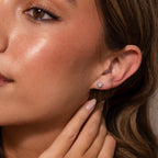 Close-up of a woman wearing Sacred Heart Studs in Silver with a sunburst texture, touching her ear with manicured fingers.