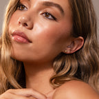 Woman with wavy light brown hair and glowing skin wears Sacred Heart Studs in 18K Gold, gazing off camera.