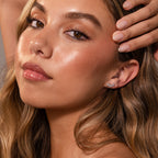 A woman with glowing skin and natural makeup touches her ear, highlighting elegant Marquise Diamond Arc Climbers in Silver adorned with shimmering marquise stones.