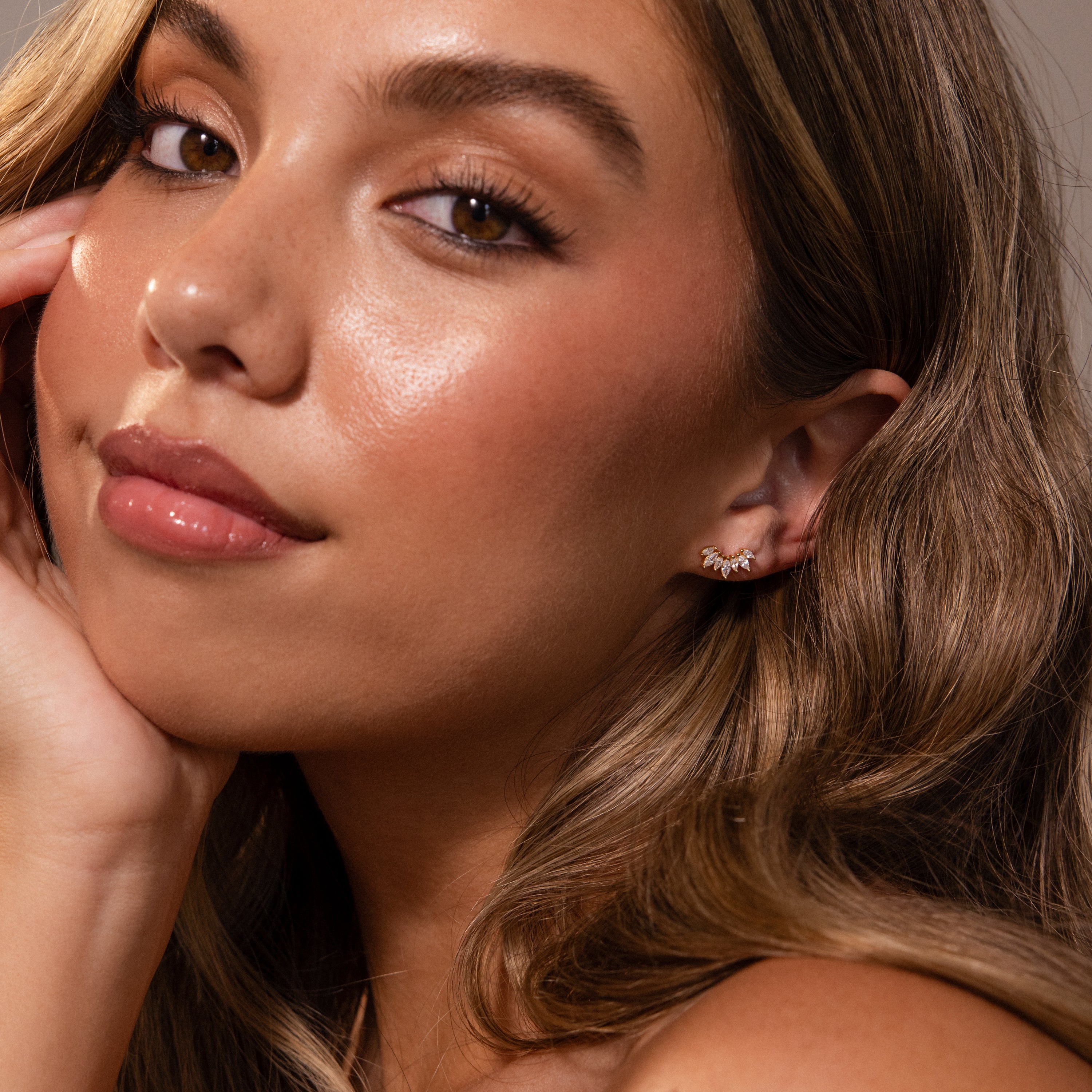 Woman with long wavy hair, glowing skin, and subtle makeup wears Marquise Diamond Arc Climbers in 18K Gold, posing thoughtfully.