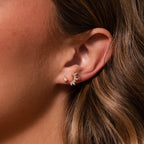 Close-up of a woman’s ear with two earrings: a small pearl stud and Marquise Diamond Arc Climbers in 18K Gold, adorned with sparkling marquise stones.