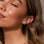 A woman with closed eyes smiles softly, wearing a gold ear cuff, textured hoop, and Marquise Diamond Arc Climbers in 18K Gold on her left ear.