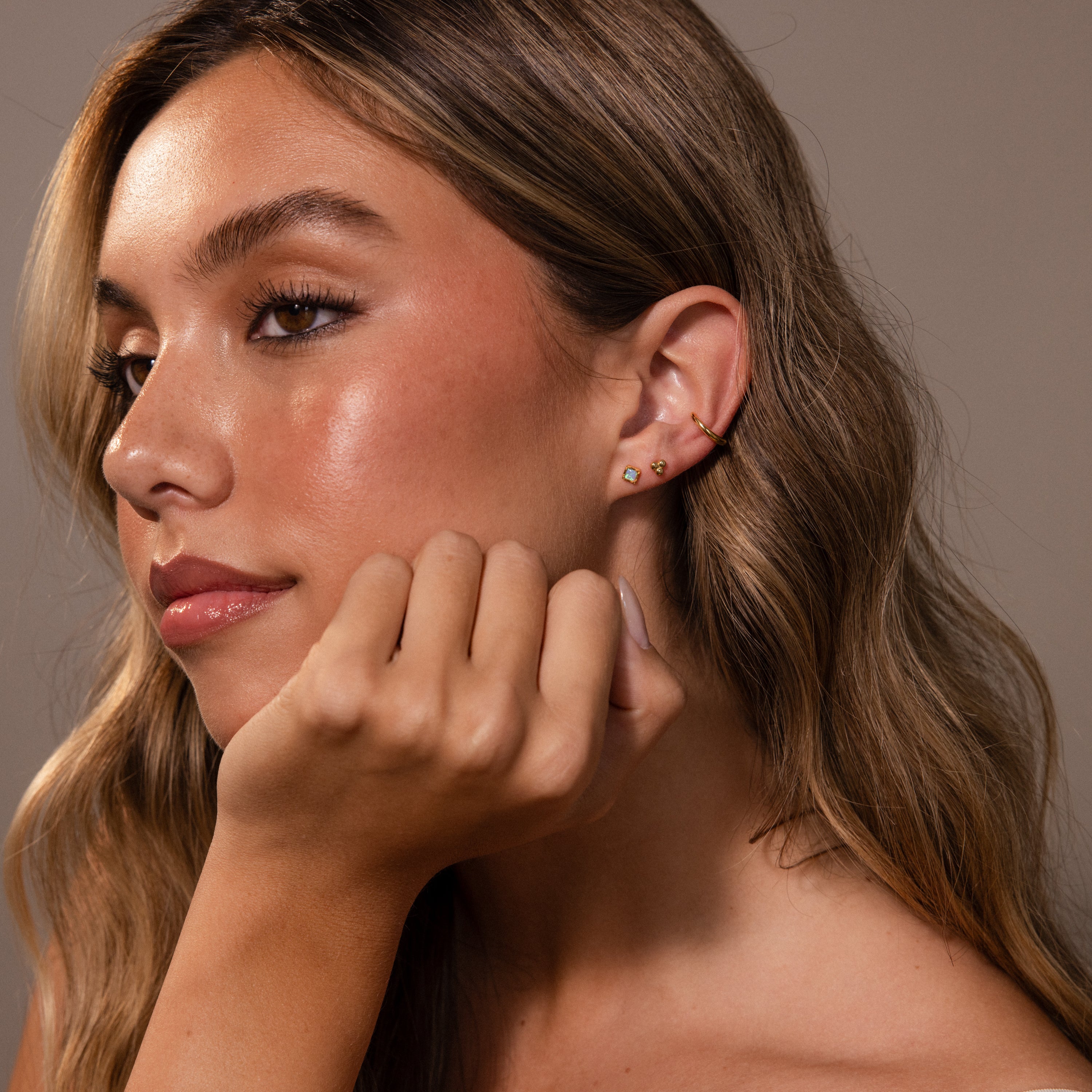 Woman with long wavy hair rests her chin on her hand, highlighting radiant skin and the elegant shimmer of Blue Opal Prism Studs for a touch of iridescent jewelry style.