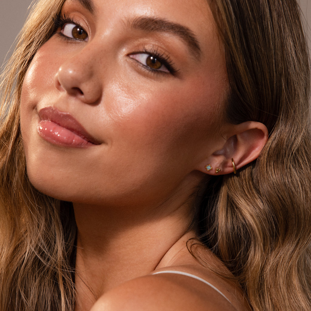 Woman with long wavy hair, glowing skin, and subtle makeup wears Blue Opal Prism Studs in 18K Gold.