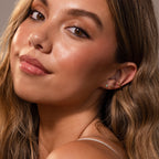 Woman with long wavy hair, glowing skin, and Blue Opal Prism Studs, looking over her shoulder and smiling softly.