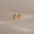 Sacred Heart Studs in 18K Gold feature a radiant sunburst texture with clear center stones, shown on a soft neutral background.