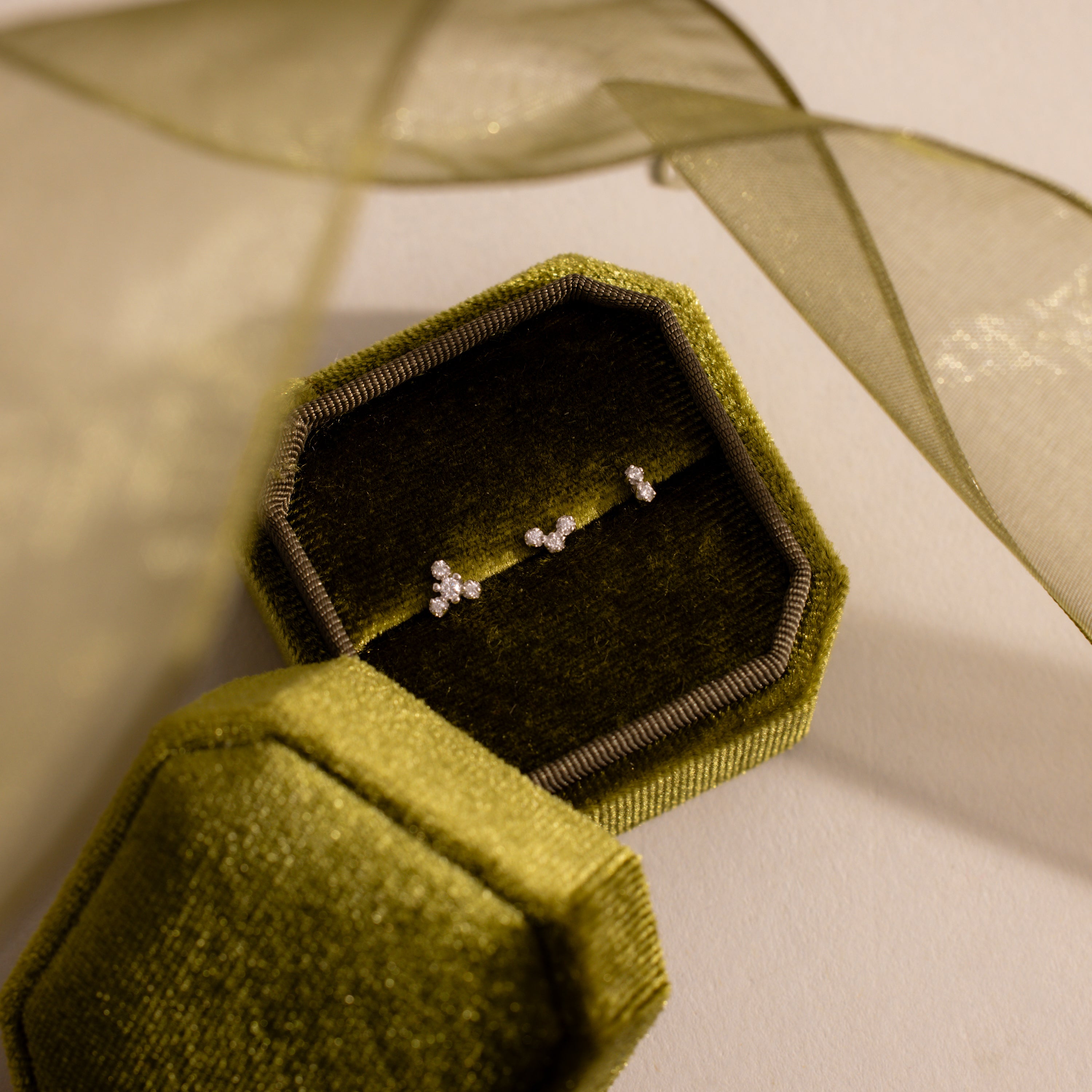 Three dainty crystal cluster flat back stud earrings in silver displayed inside an olive green velvet jewelry box.