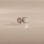 Sacred Heart Studs in Silver featuring round clear gemstones and a sunburst texture, displayed on a soft beige background.