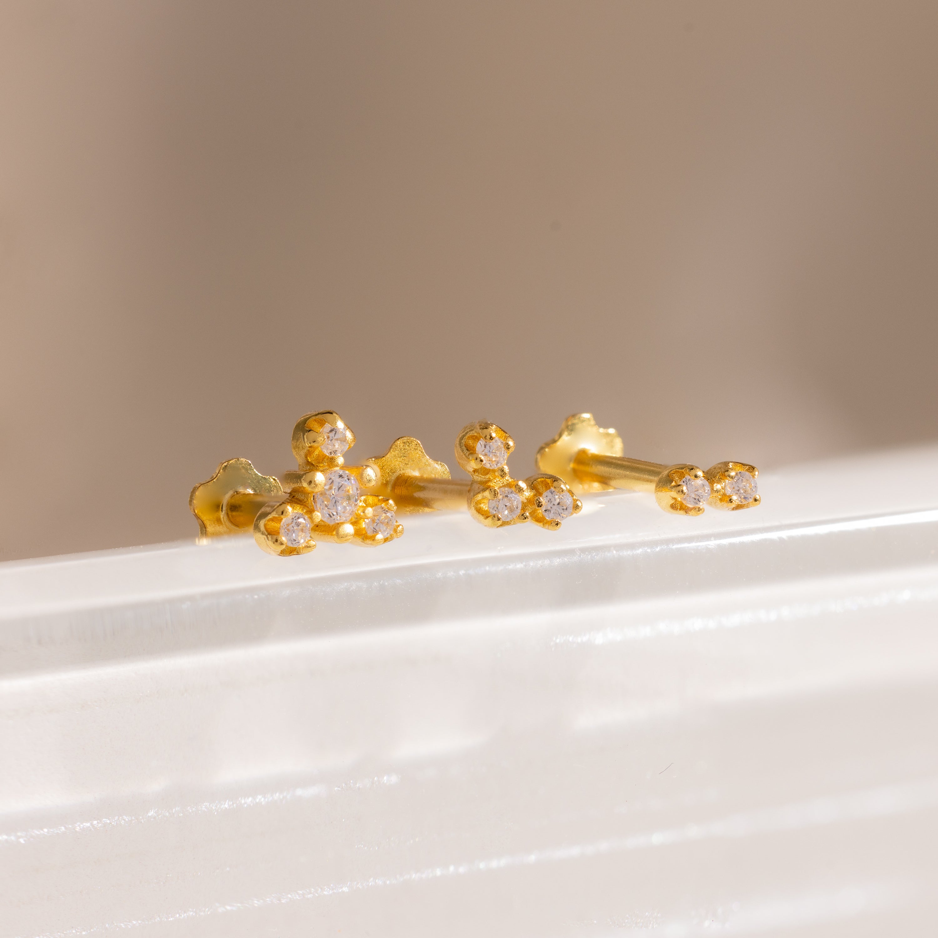 Three gold crystal cluster flat back stud earrings displayed on a white surface, featuring delicate two, three, and four stone designs.