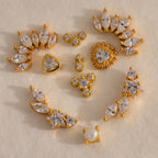 Assorted gold crystal flat back earrings featuring marquise, star, heart, pearl, and cluster designs arranged on a neutral background.