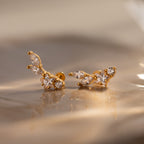 Diamond Starfall Climbers in 18K Gold, featuring marquise and round clear gemstones, are displayed on a shiny, soft beige surface.