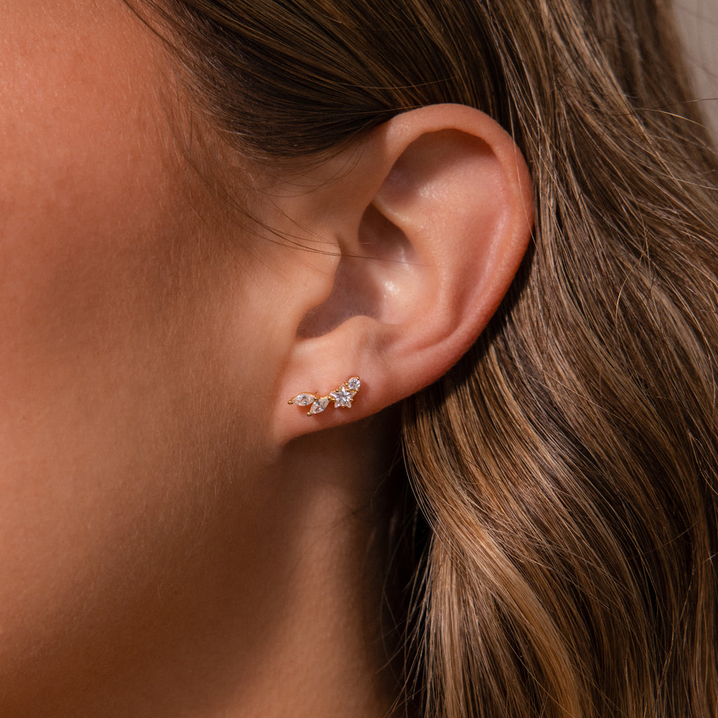 Close-up of a womans ear wearing the Diamond Starfall Climbers in 18K Gold, featuring a delicate gold ear cuff adorned with marquise cut stones.