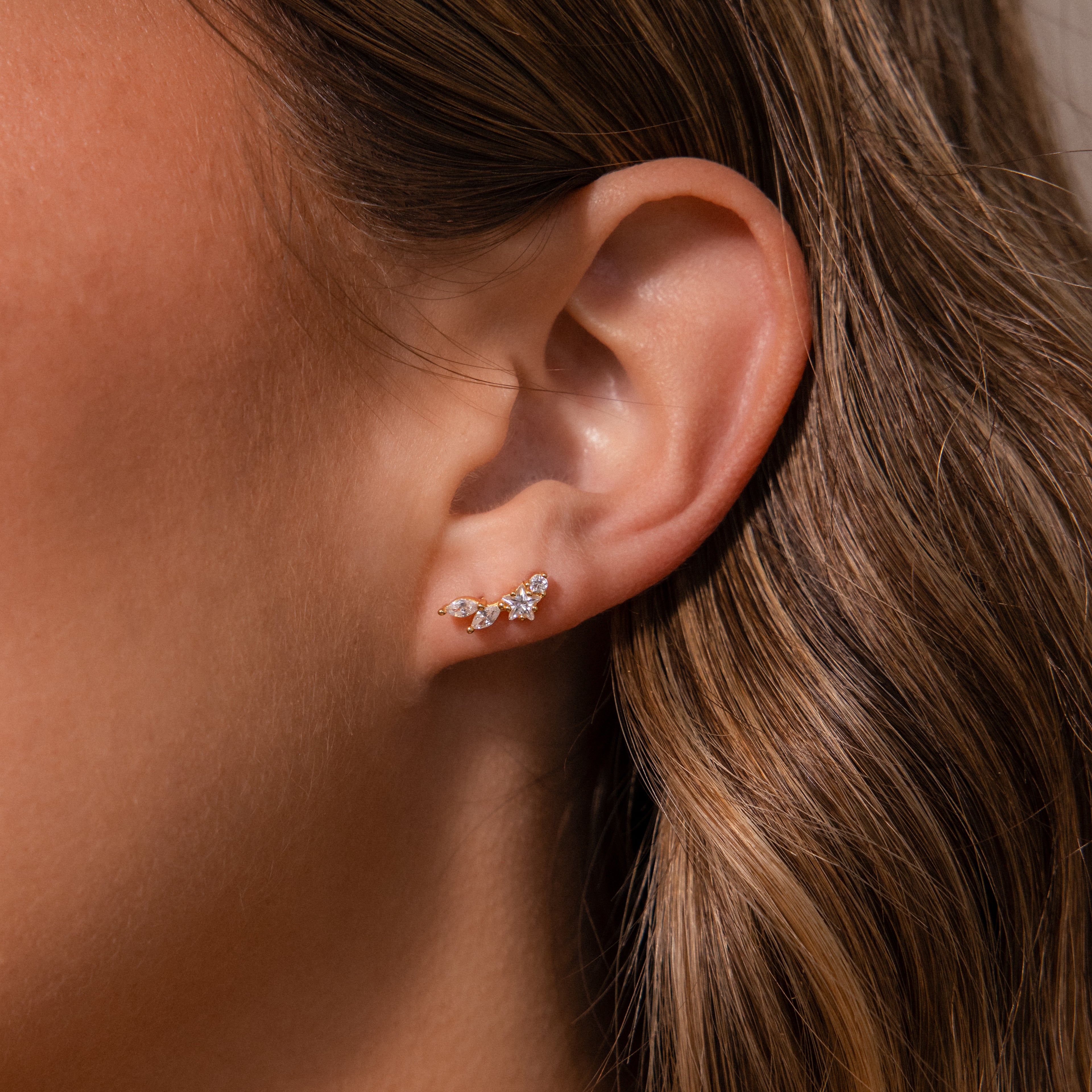 Close-up of a womans ear wearing the Diamond Starfall Climbers in 18K Gold, featuring a delicate gold ear cuff adorned with marquise cut stones.