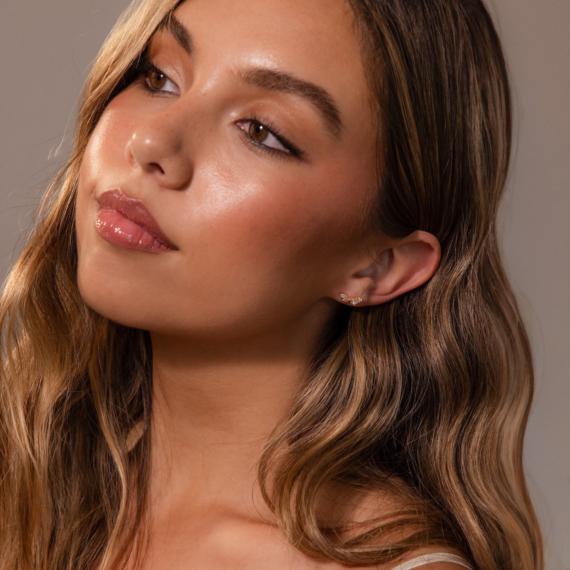 A woman with wavy light brown hair wears Diamond Starfall Climbers in 18K Gold, featuring marquise cut stones, as she gazes softly to the side against a neutral background.