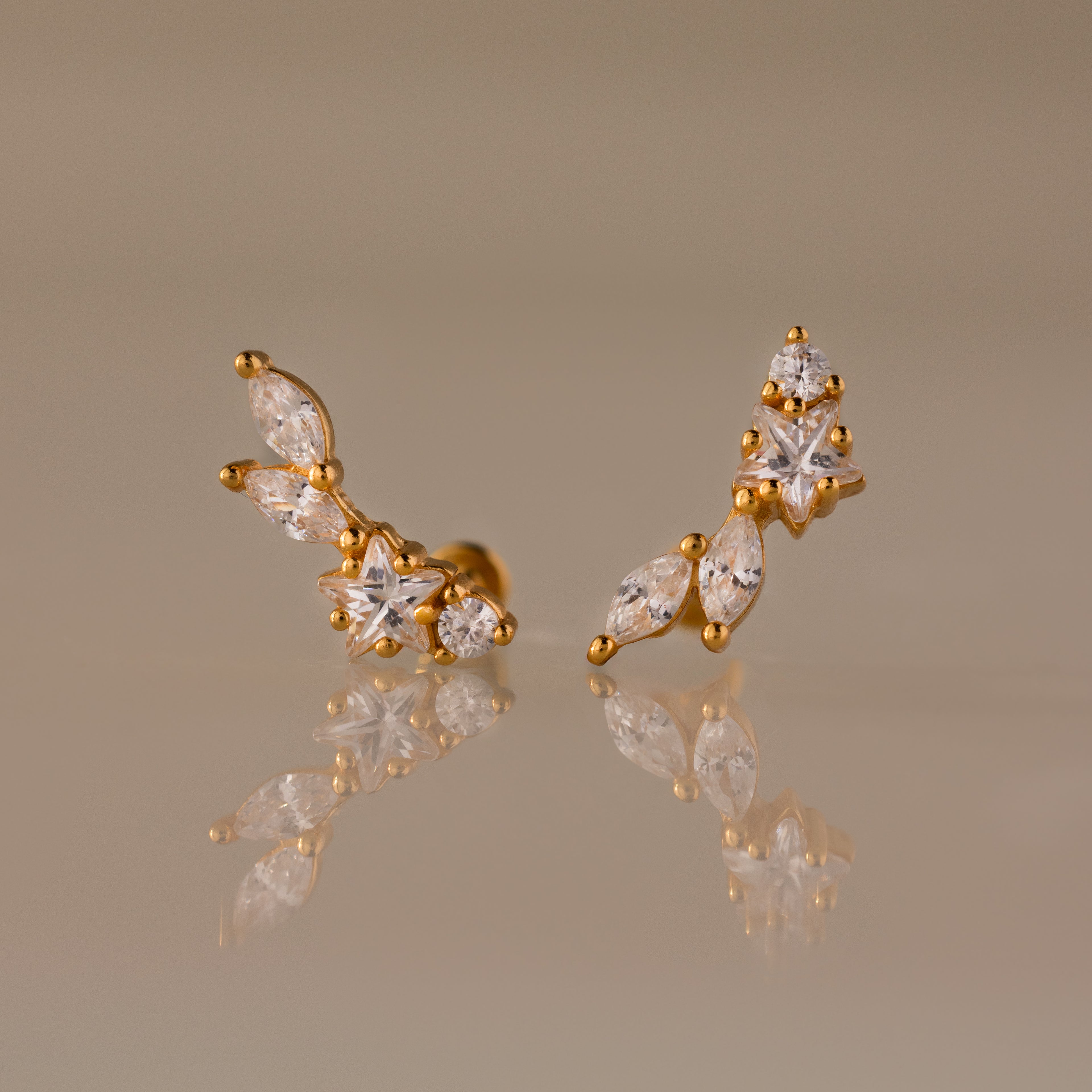 Diamond Starfall Climbers in 18K Gold, featuring marquise and round clear gemstones, elegantly displayed on a reflective beige surface.