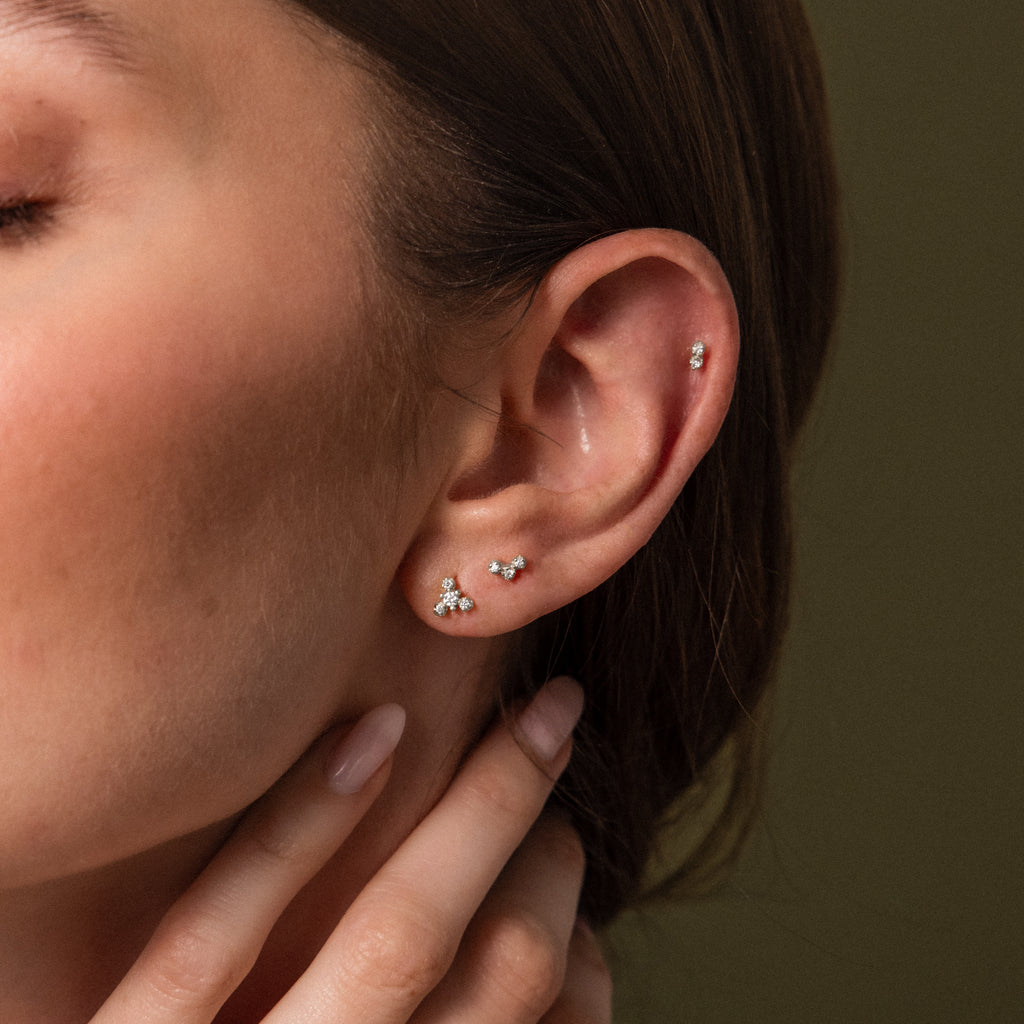 Close up of a model wearing three dainty silver crystal flat back earrings in coordinating cluster designs for a minimalist ear stack.